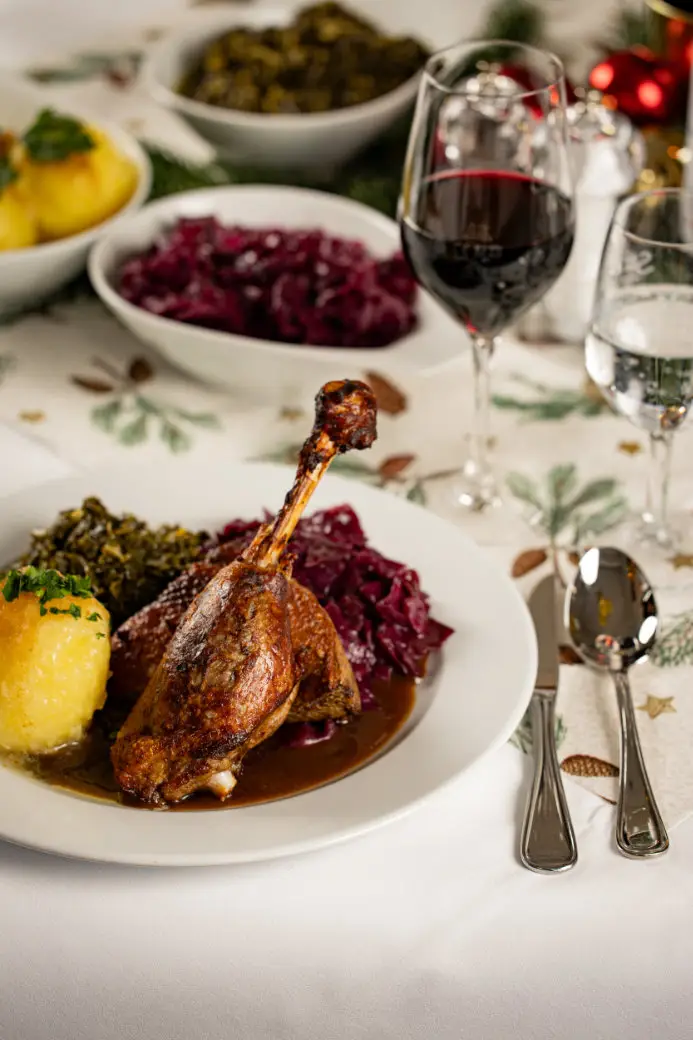 Gebratene Gänsekeule mit Rotkohl, Kartoffelklößen und Bratensauce, serviert auf einem festlich gedeckten Tisch.